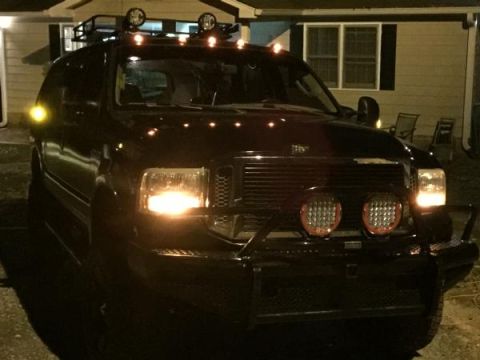 1988 Ford Bronco - A black SUV with its headlights and auxiliary lights on is parked in front of a house at night. The vehicle has a roof rack and off-road li…