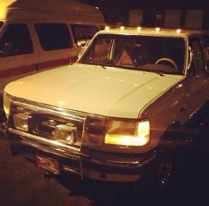 1988 Ford Bronco - The front of a white 1980s Ford pickup truck is shown at night. The truck has a large chrome grille, square headlights, and roof marker lig…