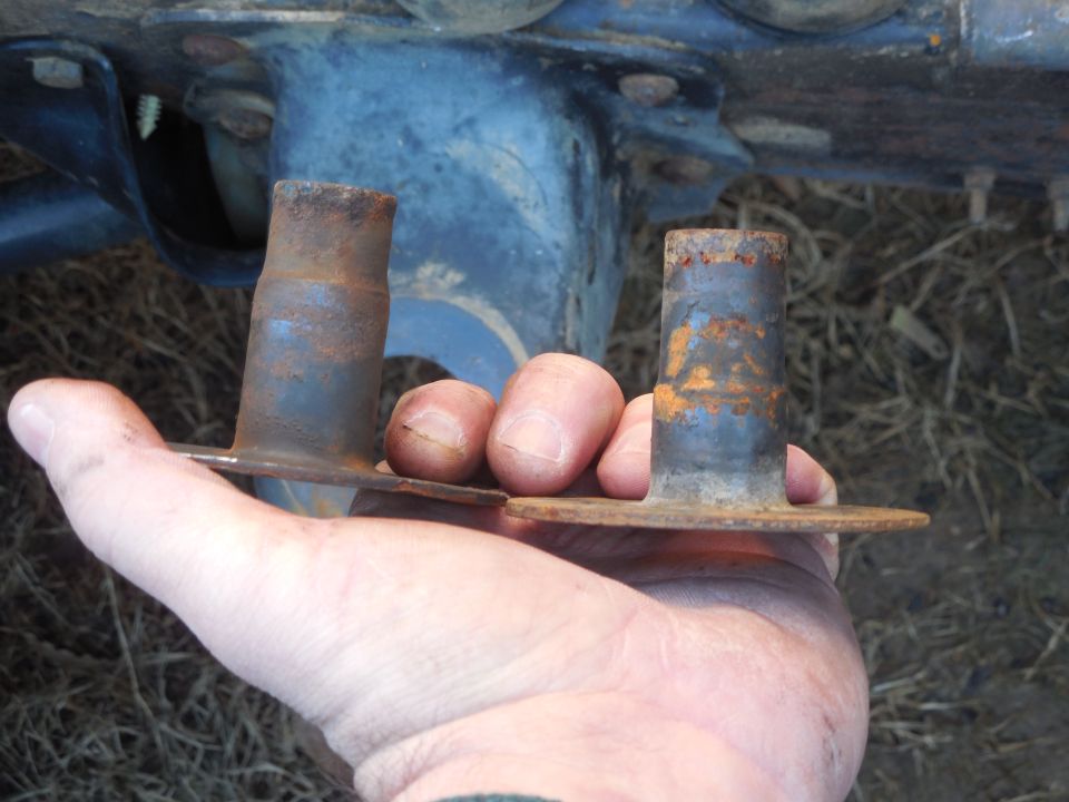 Hand holding two rusty metal sleeves under a blue Ford Bronco chassis