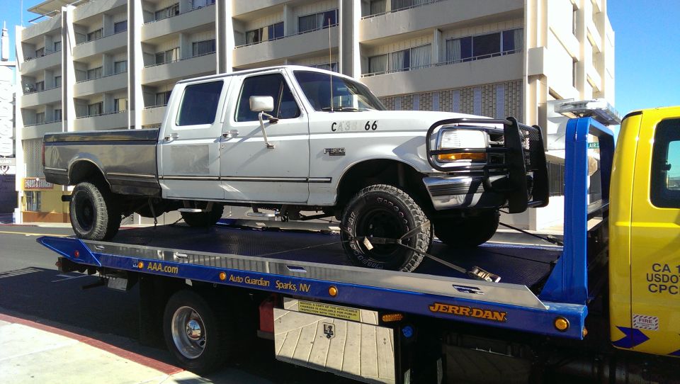 White Ford pickup truck with dark gray bed on a blue tow truck.