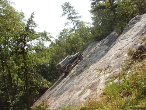 1988 Ford Bronco - A dark-colored Ford Bronco is ascending a steep, rocky incline covered in sparse vegetation. The vehicle is angled sharply upwards, with tr…