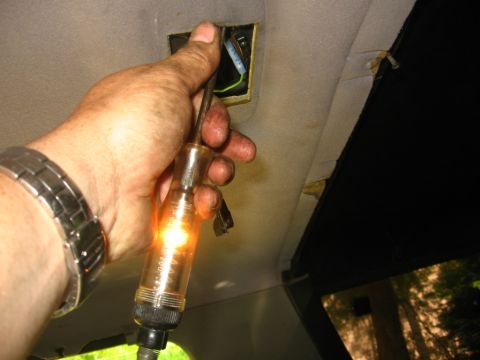 1988 Ford Bronco - A person uses a circuit tester on wiring in the vehicle's headliner.