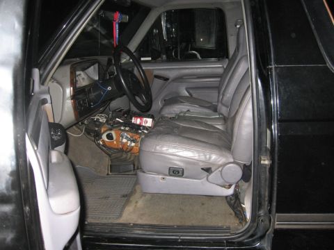 1988 Ford Bronco - The interior of a black SUV, likely from the early to mid-1990s, shows gray leather seats and a cluttered dashboard.