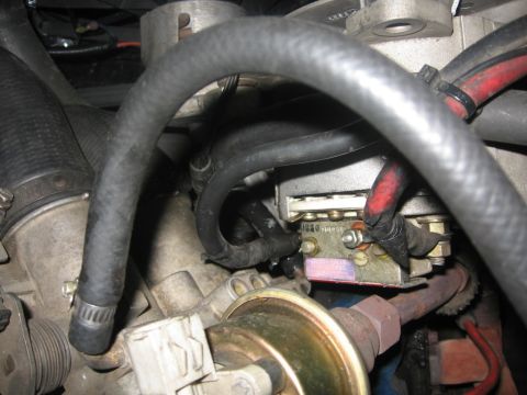 1988 Ford Bronco - A close-up view of engine components in a Ford Bronco, showing various hoses, wiring, and a metal regulator with electrical connections.