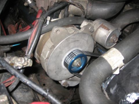 1988 Ford Bronco - A close-up view of the alternator and associated wiring in an engine bay. A blue pulley is visible on the alternator, driven by a ribbed be…