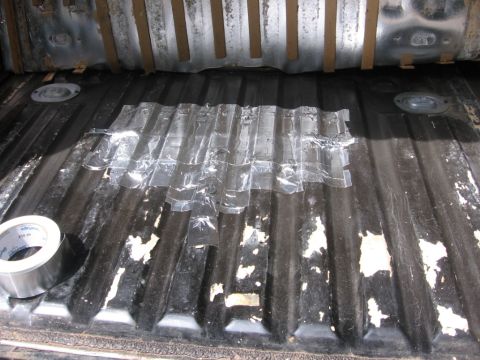 1988 Ford Bronco - The bed of a dark-colored pickup truck, likely a Ford Bronco based on context, shows a section of the bed liner covered with clear tape. A…