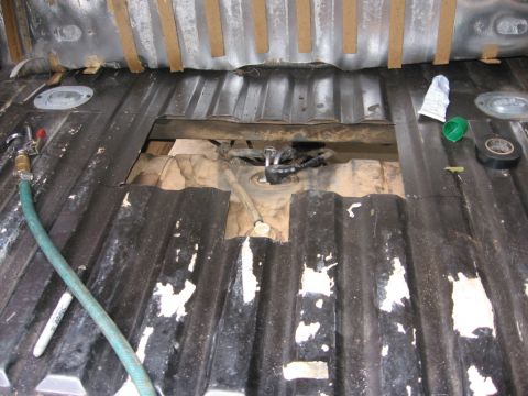 1988 Ford Bronco - The corrugated metal bed of a truck is shown with a large rectangular opening cut into it, revealing a fuel tank and associated lines below…