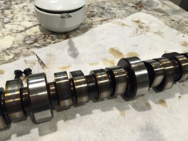 Camshaft on paper towel with bolts and a ring in a dish in the background.