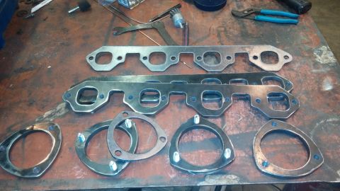 1995 Ford Bronco - Several exhaust manifold gaskets and flanges are laid out on a workbench with tools in the background.