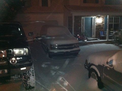 1988 Ford Bronco - Multiple vehicles are parked in a driveway and covered in snow during a winter night.