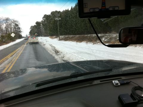 1988 Ford Bronco - A white pickup truck drives down a wet, snowy road, viewed from the perspective of another vehicle's interior.
