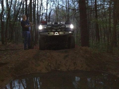 1988 Ford Bronco - A man stands near a black Ford Bronco with auxiliary lights, positioned on a dirt mound in a wooded area.