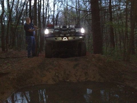 1988 Ford Bronco - A 1988 Ford Bronco navigates a muddy trail with auxiliary lights illuminating the path ahead.