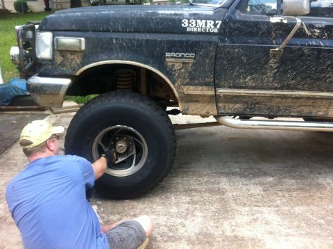 1988 Ford Bronco - A man works on a muddy black Ford Bronco, which appears to be from the late 1980s or early 1990s.