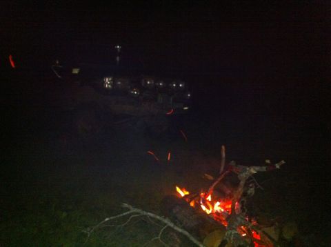 1988 Ford Bronco - A campfire burns brightly at night, with distant lights visible in the darkness.