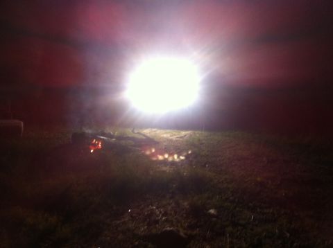 1988 Ford Bronco - A bright light illuminates a grassy area with a campfire at night.