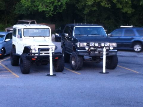 1988 Ford Bronco - Two off-road vehicles, a black Ford Bronco and a white Suzuki Samurai, are parked next to each other.