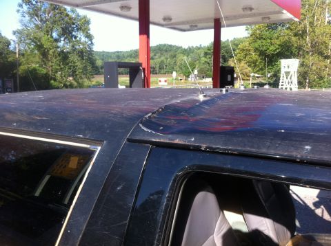 1988 Ford Bronco - The roof of a dark SUV shows significant damage and wear under a gas station canopy.