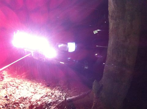 1988 Ford Bronco - A vehicle with powerful lights navigates a rough, wooded terrain in the dark.