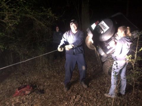 1988 Ford Bronco - A Jeep is being pulled from a wooded area at night with the help of several people.