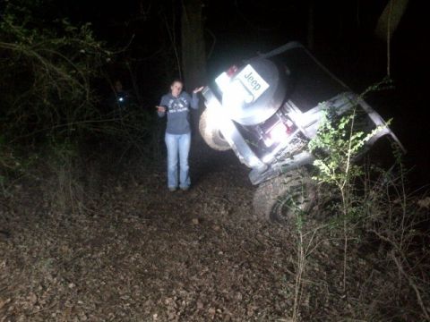 1988 Ford Bronco - A Jeep is seen tilted on its side in a wooded area at night, with a person standing next to it.