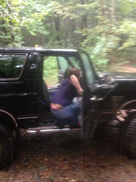 1988 Ford Bronco - Person entering a black 1988 Ford Bronco in a wooded area.