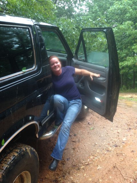 1988 Ford Bronco - A woman exits a black SUV on a muddy, wooded road.
