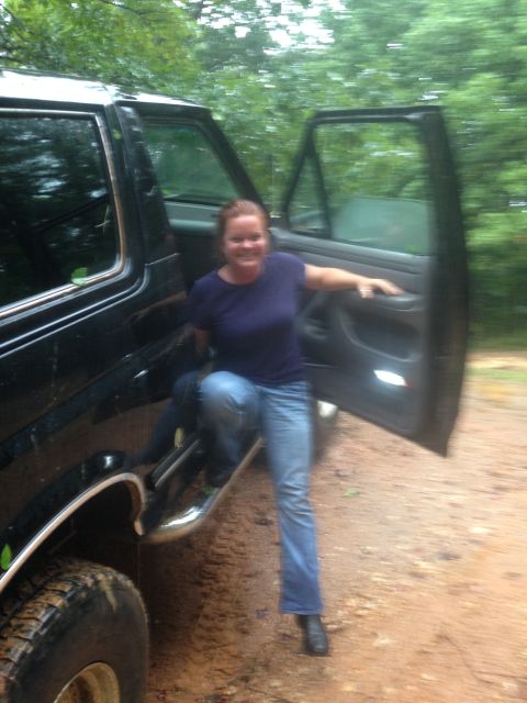 1988 Ford Bronco - A woman exits a black SUV on a dirt road surrounded by trees.