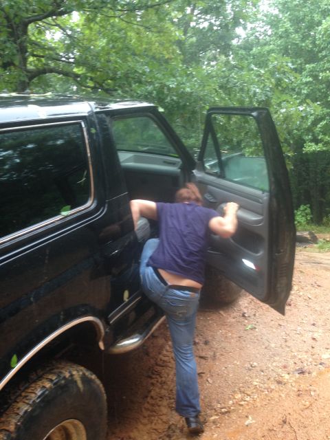 1988 Ford Bronco - A person enters a black SUV parked on a dirt road surrounded by trees.