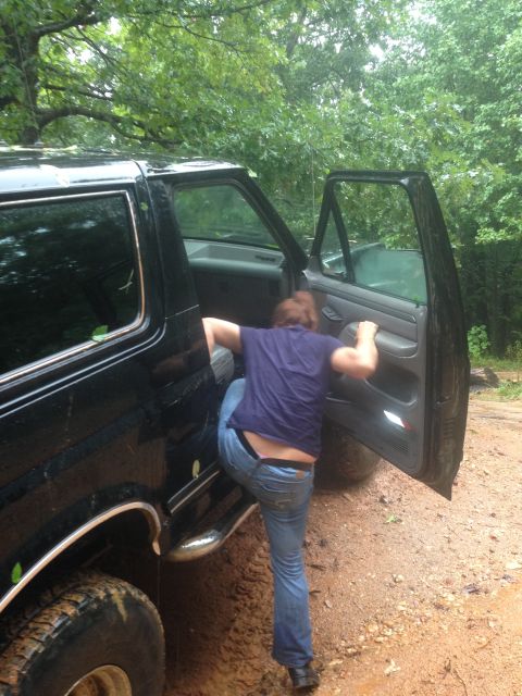 1988 Ford Bronco - A person climbs into a black 1988 Ford Bronco, which appears to be stuck in mud.