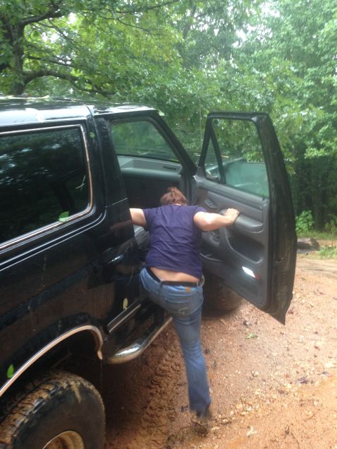 1988 Ford Bronco - Person entering a black SUV parked off-road in muddy conditions.