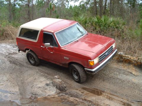 1995 Ford Bronco - This red Ford Bronco is navigating a muddy, off-road trail.