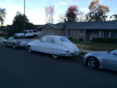 1968 Ford Mustang - A white vintage sedan is parked curbside, with other vehicles nearby under a dusky sky.