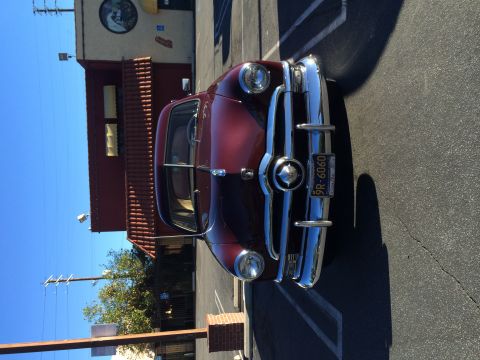 1968 Ford Mustang - A vintage maroon sedan with a prominent chrome grille is parked in a lot under a clear blue sky.