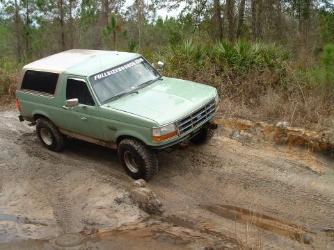1995 Ford Bronco - A green 1995 Ford Bronco navigates a muddy off-road trail.