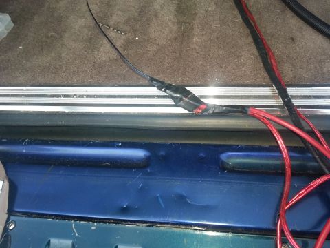1994 Ford Bronco - Photo of red power and black ground cables routed over a metal door sill during a car-audio install.