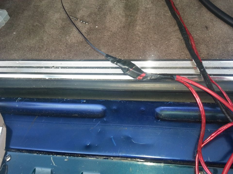 Power and ground cables routed over a metal door sill during audio install