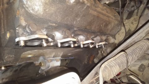 1995 Ford Bronco - A close-up view of the exhaust manifold area of a vehicle, showing newly installed exhaust manifold spacers with bolts. The engine componen…
