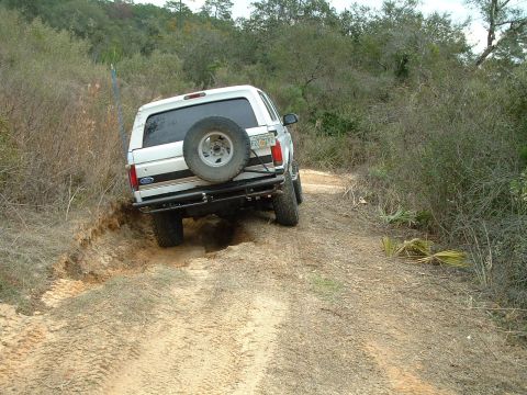 1995 Ford Bronco - White SUV navigates a challenging off-road trail with steep inclines and loose dirt.