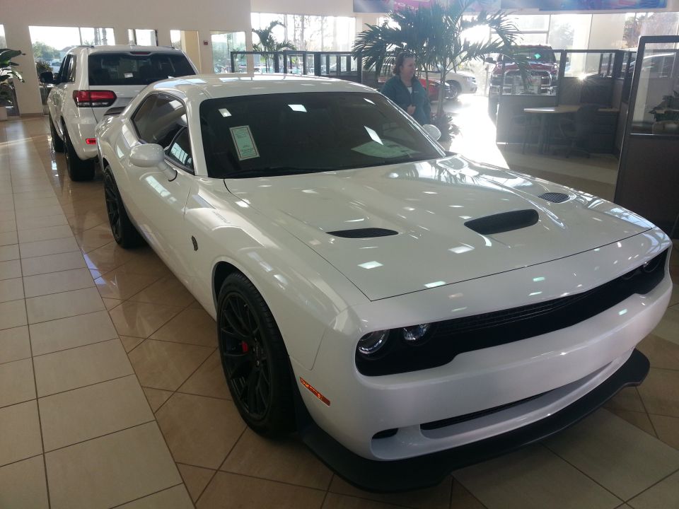 White Dodge Challenger parked indoors, front 3/4 view, with a white SUV behind it.