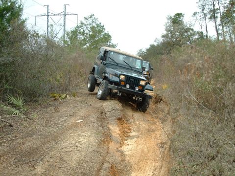 1995 Ford Bronco - A black Jeep Wrangler navigates a challenging dirt path, with another vehicle following closely behind.