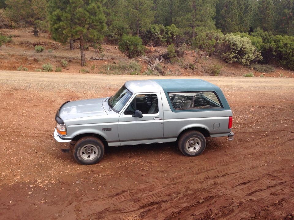 Silver Ford Bronco with a green top parked on a dirt road