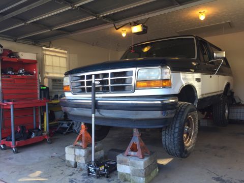 1994 Ford Bronco - Ford Bronco with a two-tone paint scheme is elevated on jack stands inside a garage.