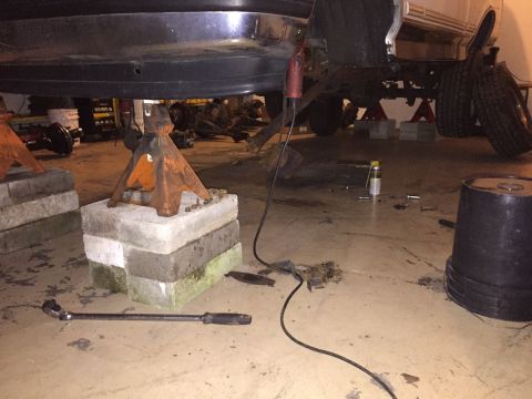 1994 Ford Bronco - A vehicle is elevated on jack stands in a garage, surrounded by tools and parts, indicating ongoing maintenance or repair.