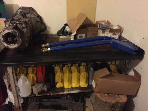 1994 Ford Bronco - A transmission and a pair of blue control arms are displayed on a shelf above containers of oil.