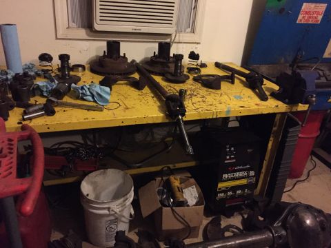 1994 Ford Bronco - A collection of vehicle parts, including hubs, rotors, and a driveshaft, are laid out on a yellow workbench.