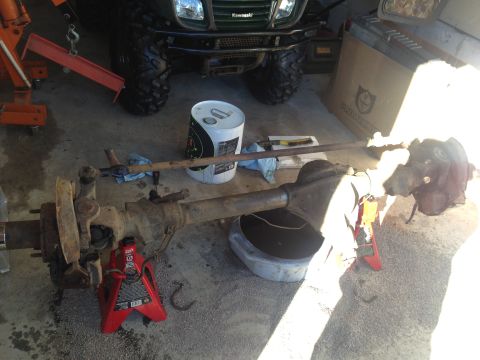 1994 Ford Bronco - Front axle assembly removed from a vehicle, resting on jack stands with a drain pan below.