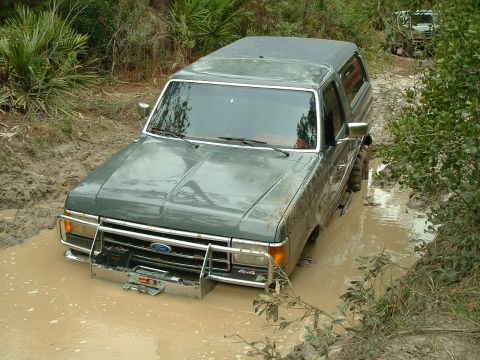 1995 Ford Bronco - A gray Ford Bronco is stuck in a muddy rut with another vehicle in the background.