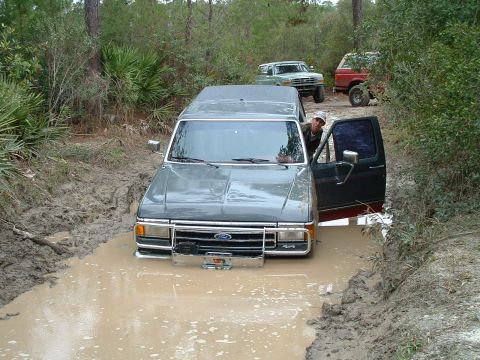 1995 Ford Bronco - A 1995 Ford Bronco is stuck in a muddy ditch, with two other trucks visible in the background.
