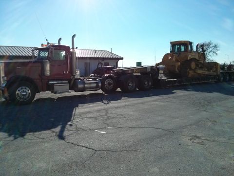 1986 Ford Bronco - A maroon semi-truck is parked next to a yellow bulldozer loaded onto a flatbed trailer.